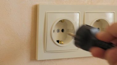 Kablolu siyah bir elektrik prizi elle beyaz bir sokete yerleştirilir.