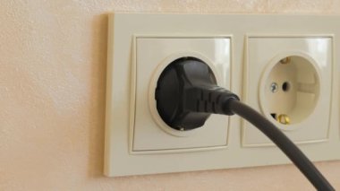 Kablosu olan siyah bir elektrik prizi beyaz bir prizden elle çıkarılır..