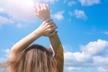 Mavi bulutlu arka planda genç kadın elleri yakın çekim. Parlak yaz güneşi. Kurtuluş, özgürlük, aşk ve bağımsızlık kavramı