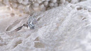 Beyaz örgü ve çiçek arkaplanındaki elmas yüzüğü kapat. Aşk, sevgililer günü, ilişki ve düğün konsepti. Yumuşak ve seçici odak.