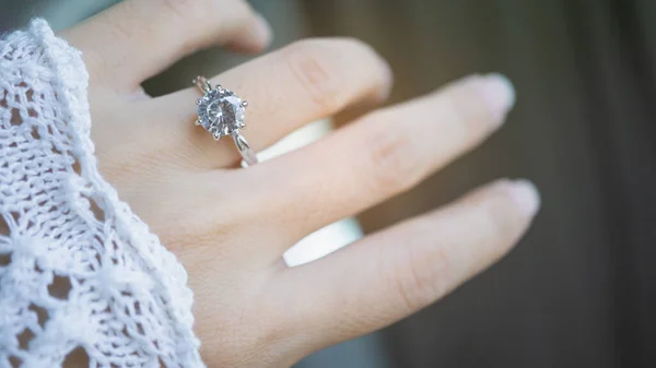 Close up of an elegant diamond ring on woman finger with sunlight and shadow background. love and wedding concept. Soft and selective focus.