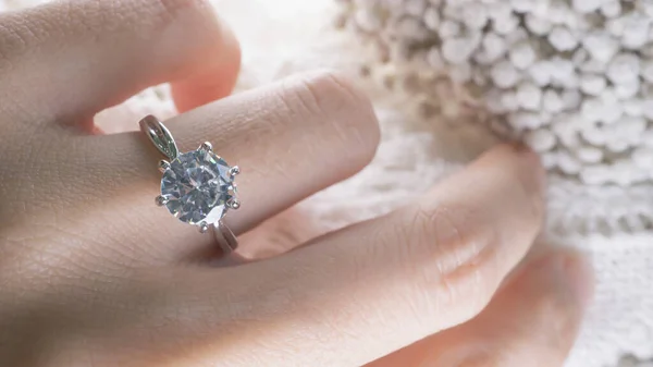 Close up of an elegant diamond ring on woman finger while touching the flower with sunlight and shadow background. love and wedding concept. Soft and selective focus.