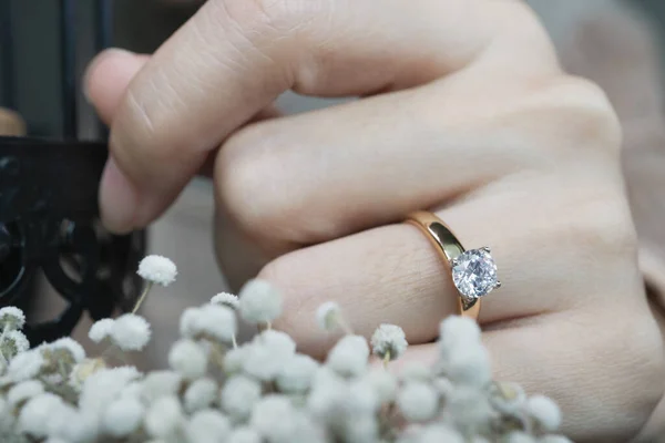 Close up of an elegant diamond ring on woman finger while touching the flower with sunlight and shadow background. love and wedding concept. Soft and selective focus.