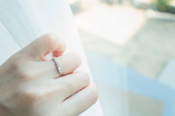 Close up of an elegant diamond ring on woman finger with sunlight and shadow background. love and wedding concept. Soft and selective focus.