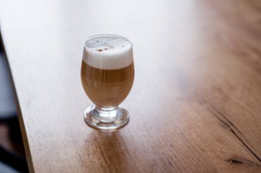 Süt katmanlı sütlü kahve, yüksek bardakta, ahşap bir masada.. 