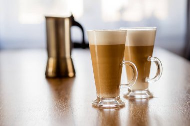 Bardakta iki sütlü macchiato kahve, ahşap masada köpük, moka pot, ev yapımı..