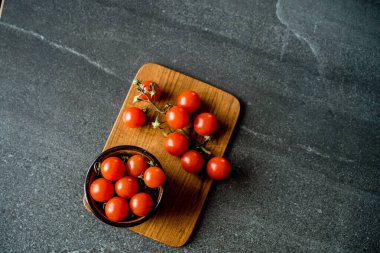 Koyu renkli arkaplanda kırmızı kiraz domatesleri ve tahta kesme tahtası.. 