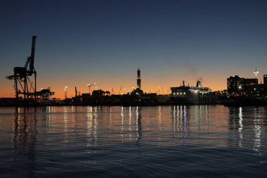 Cenova, İtalya - 22 Şubat 2022: Cenova (Cenova) limanının iskele vinçleri ve sanayi bölgesi ile akşam manzarası. Ceneviz, İtalya. Geceleri fener ışıkları. Şehir denizin arkasında aydınlandı..