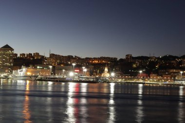 Cenova, İtalya - 22 Şubat 2022: Cenova (Cenova) limanının iskele vinçleri ve sanayi bölgesi ile akşam manzarası. Ceneviz, İtalya. Geceleri fener ışıkları. Şehir denizin arkasında aydınlandı..