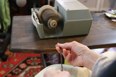 Bir kadın elektrikli çarkla örgü örmek için iplik yapar..