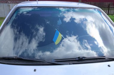 Ukrayna bayrağı bir arabanın ön camına asılmış. Bulutlarla yansıtılan gökyüzü.