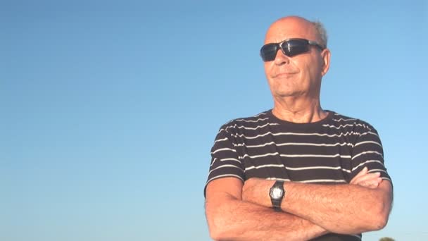 El hombre mayor mira al otro lado del océano. Reflexión en gafas de sol — Vídeos de Stock