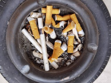 Sigara küllüğü. Bir arabanın tekerinde yanmış çöpler. Sağlıksız.