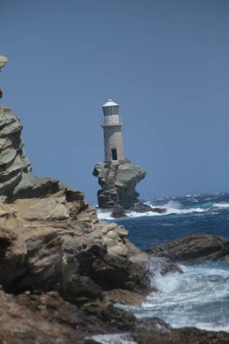 lighthouse in andros island greece in day light and sea waves in a windy day
