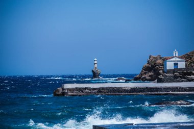 lighthouse in andros island greece in day light and sea waves in a windy day