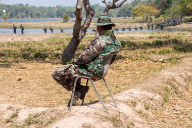 Ormanın arka planında silahlı kamuflaj üniformalı bir adam.