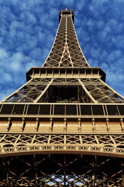 Paris'te Eyfel Kulesi ile yeşil çimen, mavi gökyüzü ve beyaz bulutlar