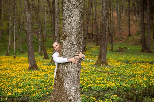 Um homem feliz abraçando uma árvore na floresta — Fotografia de Stock