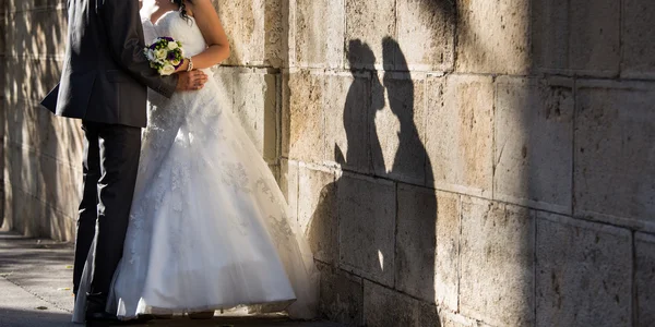 Bruden och brudgummen nära väggen med skugga — Stockfoto