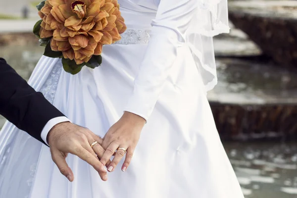 Bruidspaar hand in hand met water op achtergrond — Stockfoto