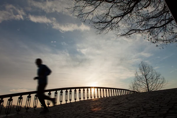 Silhueta do homem correndo ao nascer do sol na ponte — Fotografia de Stock