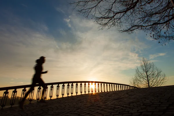 Silhueta da menina que corre ao nascer do sol na ponte — Fotografia de Stock