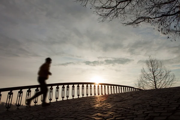 Silhueta do homem correndo ao nascer do sol na ponte — Fotografia de Stock