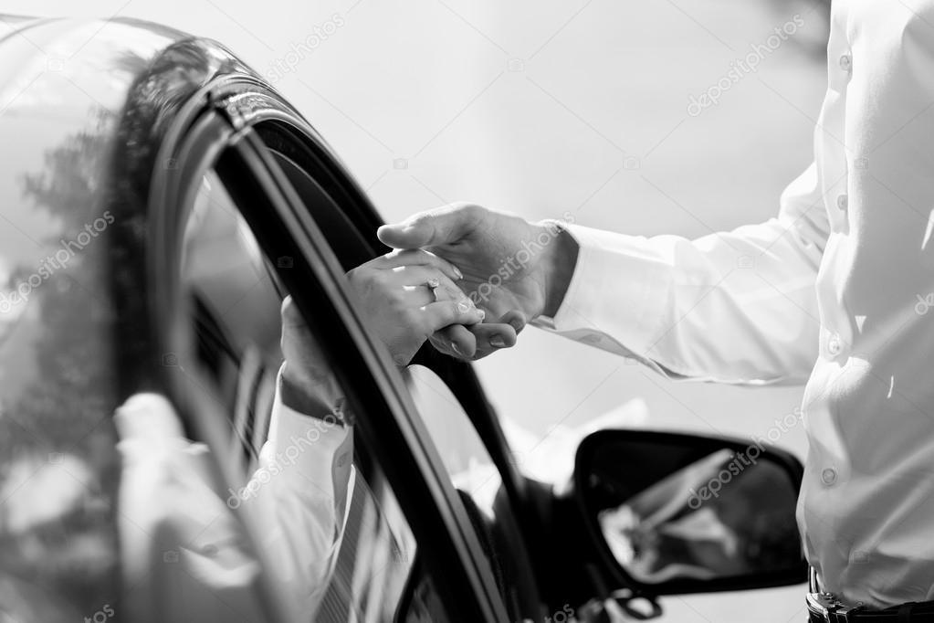 Gentle holding hands near car with wedding couple with ring blac