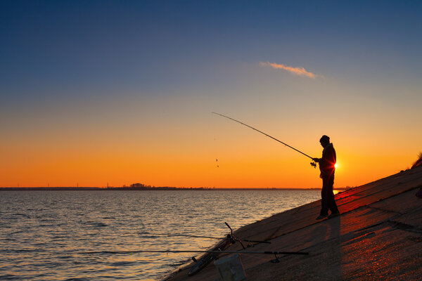 Силуэт рыбаков на берегу реки против заката
