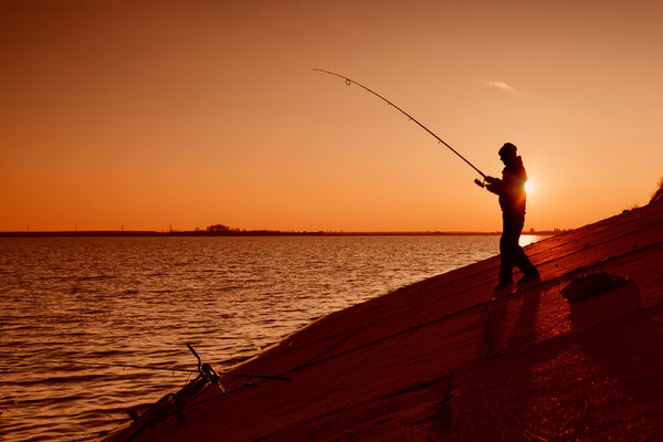 Силуэт рыбаков на берегу реки против заката
