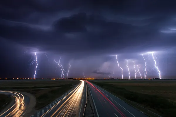 พายุฝนฟ้าคะนองและฟ้าผ่าในเวลากลางคืนเหนือทางหลวงที่มีเอ็นรถ — ภาพถ่ายสต็อก