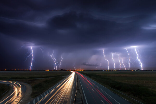 Thunderstorm and lightnings in night over a highway with car lig