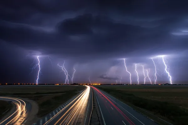 Thunderstorm and lightnings in night over a highway with car lig Royalty Free Stock Photos
