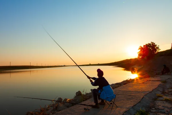 年轻人与丰富多彩的背景衬托的湖面上钓鱼 — 图库照片