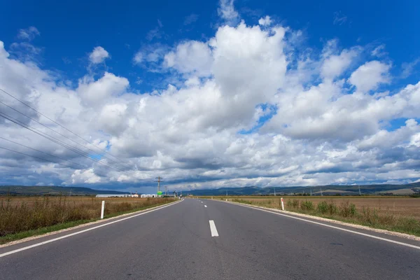 Uma estrada rural sob um céu azul brilhante . — Fotografia de Stock