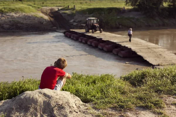 Child looking at bridge over river with tractor in background — Stock Photo, Image