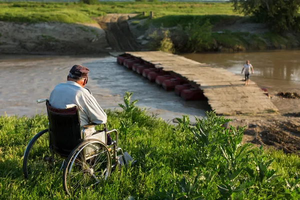 Pensionerad person i rullstol beundra bron över floden — Stockfoto