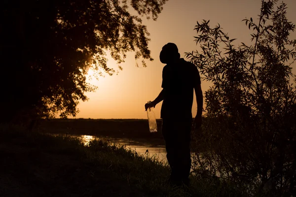 Silhouet van de mens bij zonsondergang met fles alcohol in struiken — Stockfoto