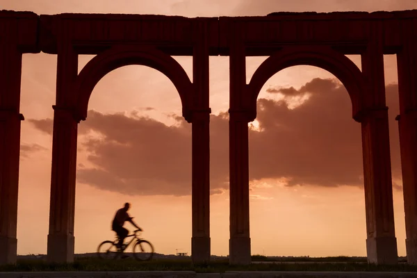 Sylwetka rowerzysta rozmowy na telefon pod kolumny w zachód słońca — Zdjęcie stockowe
