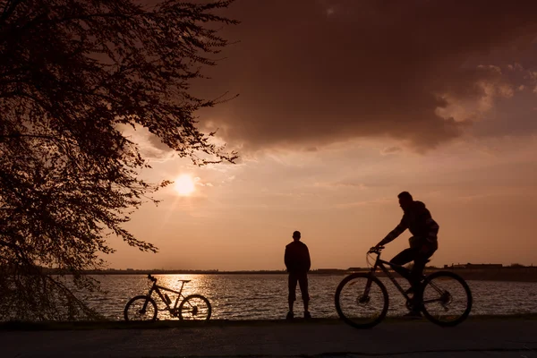 Imagem do motociclista admirando o pôr do sol no lago — Fotografia de Stock