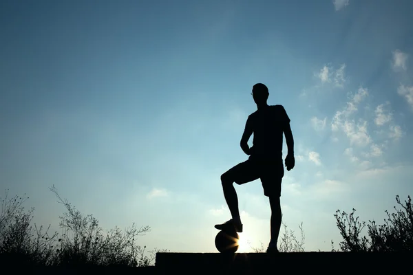 Силуэт футболиста, отдыхающего ногой на мяче — стоковое фото