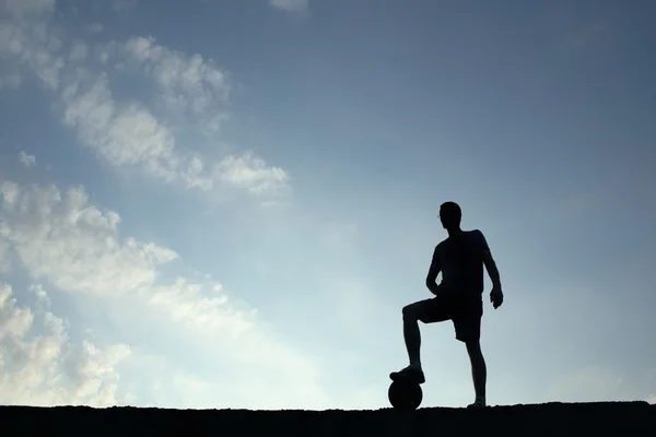 足のボールの上で休んでサッカー男のシルエット — ストック写真