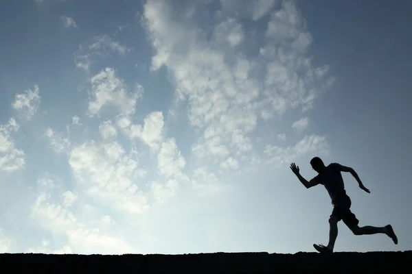 Silhouette des Sportlers läuft mit blauem Himmel und Wolken auf dem Rücken — Stockfoto