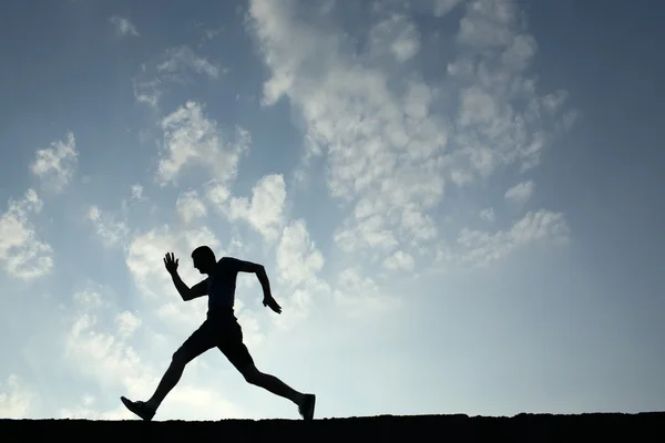 Силуэт спортсмена, бегущего с голубым небом и облаками на спине — стоковое фото