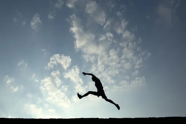 Silhouette des Sportlers springt mit blauem Himmel und Wolken auf dem Rücken — Stockfoto