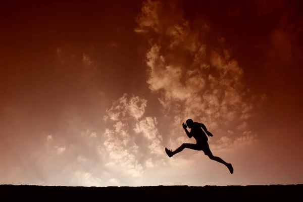 Silhouette des Sportlers springt mit blauem Himmel und Wolken auf dem Rücken — Stockfoto