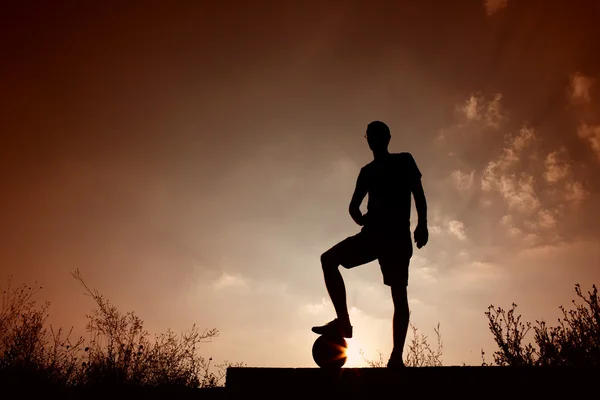 足のボールの上で休んでサッカー男のシルエット — ストック写真