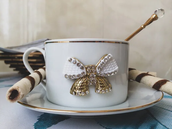 White vintage cup with gold and bow on saucer, spoon, crystal, kitchen, light, background, beautiful, exquisite, expensive, drink