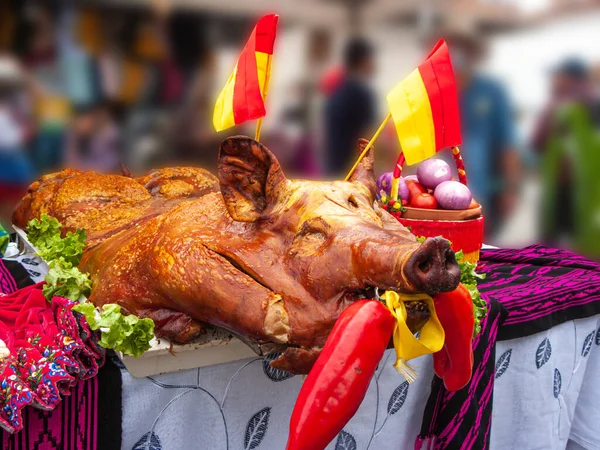Big whole roasted pig (chancho) decorated in colors of flag of Azuay is on the table and ready for sale at the open market in Cuenca. Street food. Traditional food and the way to cook pigs in Ecuador
