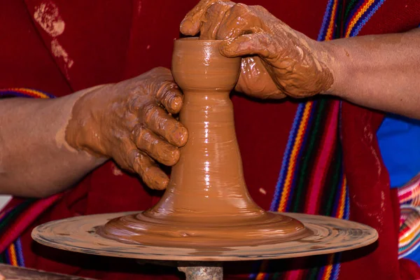Close up mud covered hands of adult ecuadorian man making a cup of clay on a potter\'s wheel. Man dressed in traditional poncho